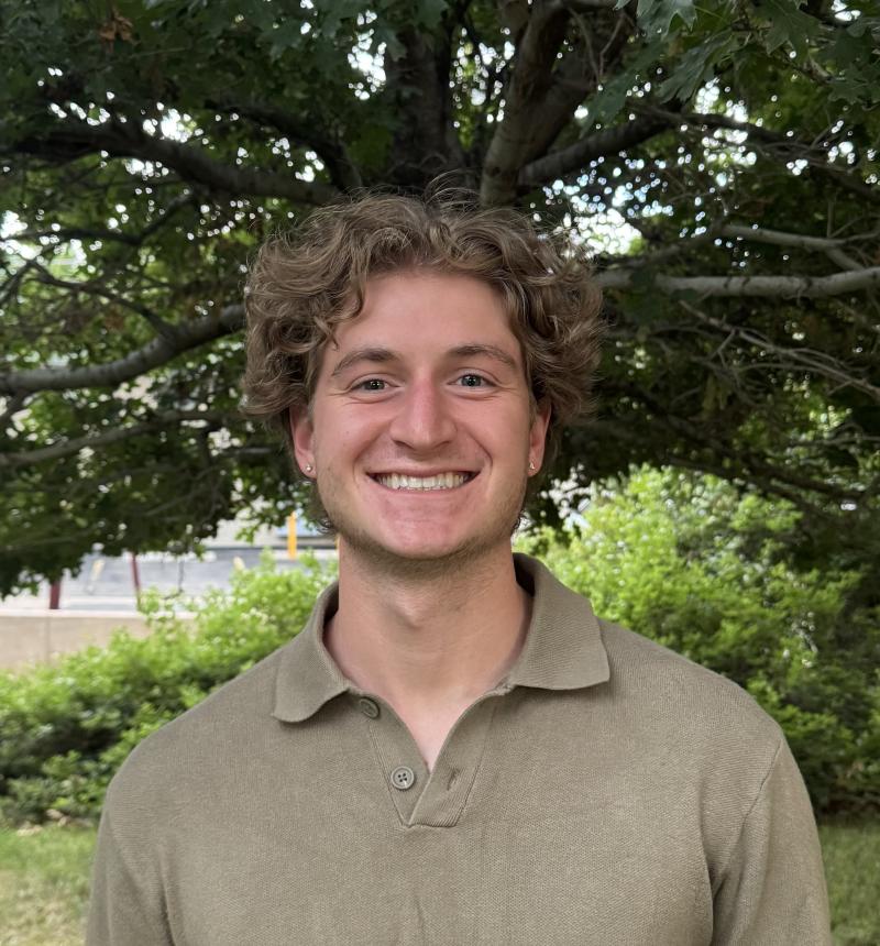 Young man smiles in front of a tree