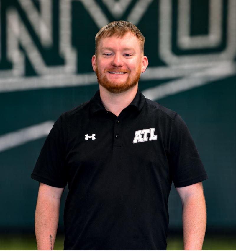 Young man smiles in front of a sports banner