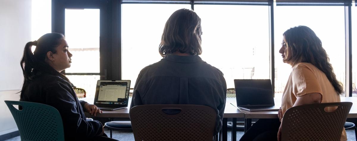 three women at a conference desk, silhouetted from behind