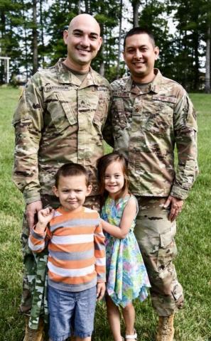 two men in miltary uniforms standing with two children standing in front of them
